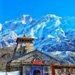 Historic Kedarnath Temple amidst stunning snow-capped Himalayan peaks on a clear day.